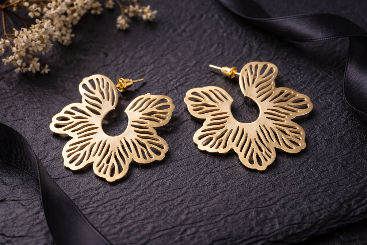 Gold floral earrings on a dark textured surface with dried flowers and black ribbons.
Color: Gold
