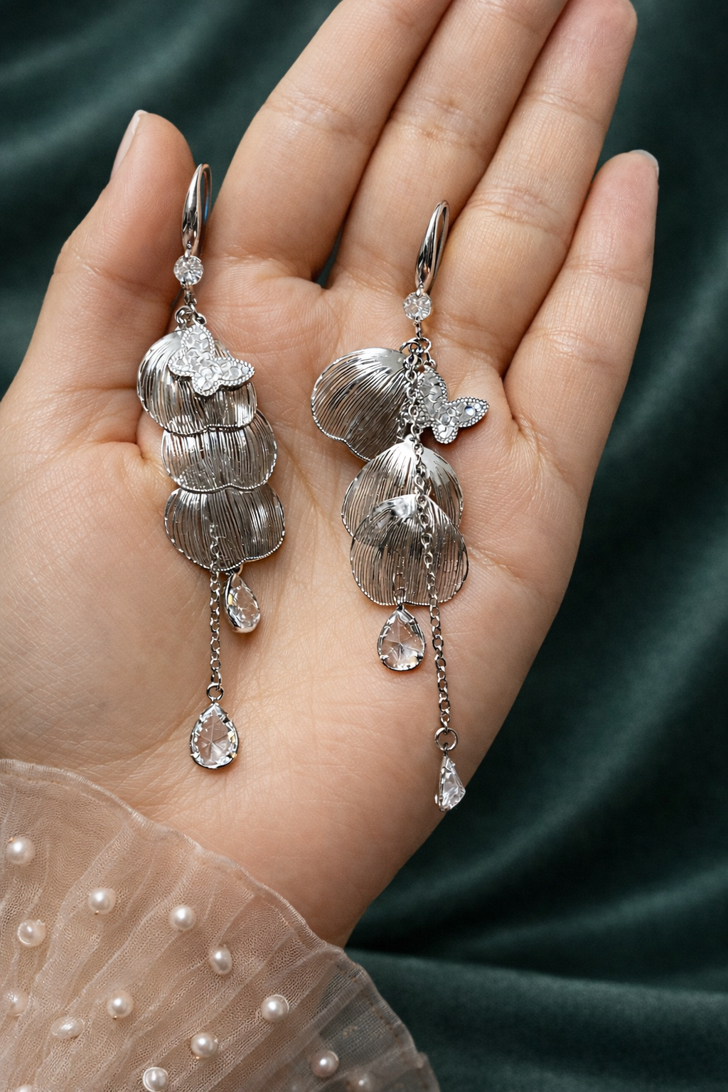 Anti-Tarnish, Ashaarya, Ashaarya Jewels, Ashaarya Jewellery, Silver earrings with gemstones held in a hand against a dark green fabric background