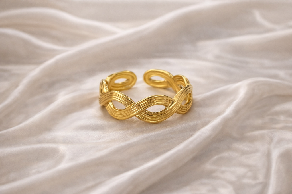 Anti-tarnish gold adjustable twist ring with infinity rope design, open back for flexible sizing, displayed on hand against satin background — lightweight comfort jewellery by Ashaarya. Gold bracelet on a textured beige fabric background