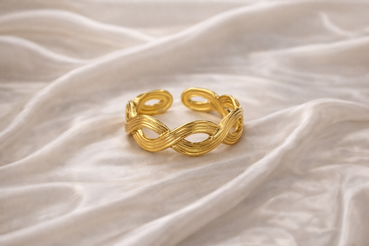 Anti-tarnish gold adjustable twist ring with infinity rope design, open back for flexible sizing, displayed on hand against satin background — lightweight comfort jewellery by Ashaarya. Gold bracelet on a textured beige fabric background