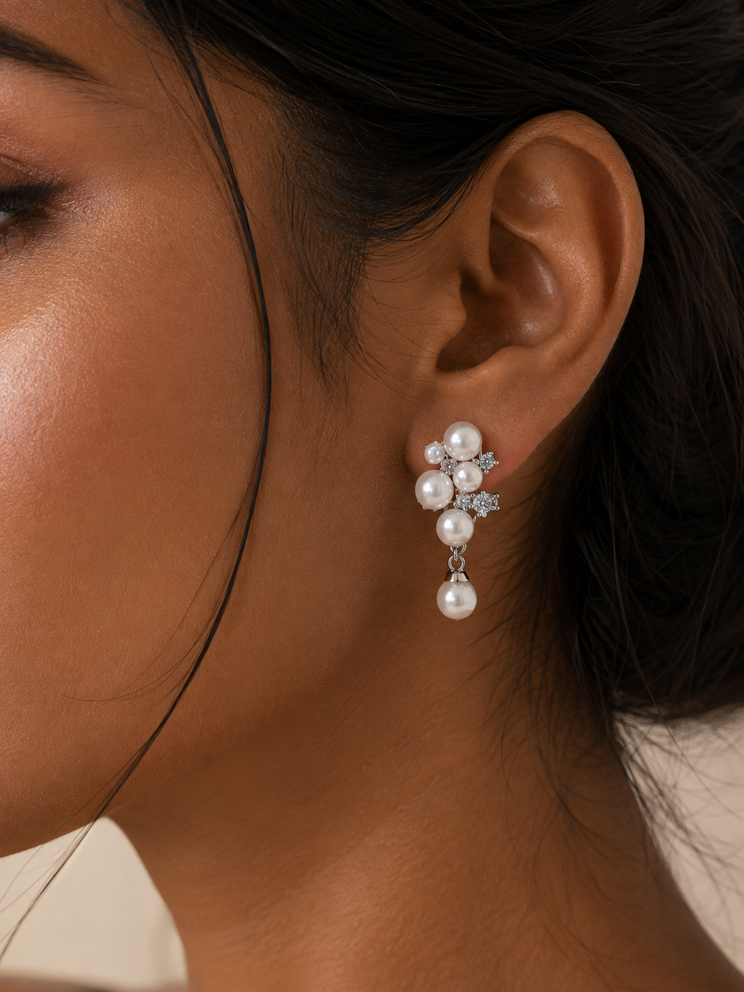 A close-up of a woman's ear wearing a dangling pearl clip n earring with silver-toned floral details and clear stones. 