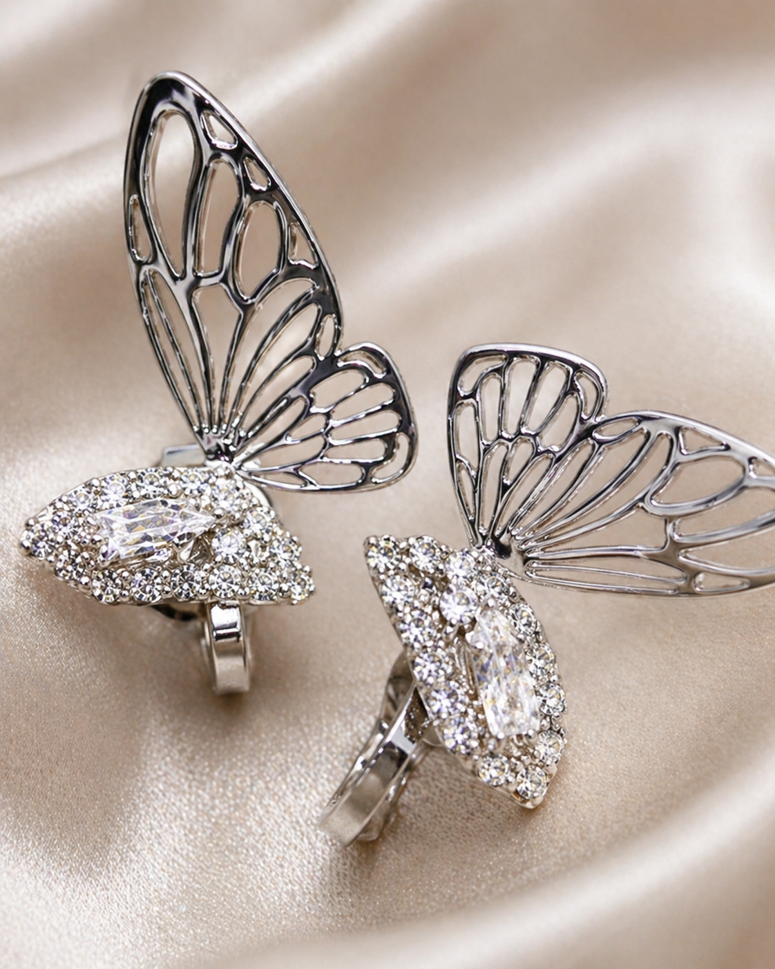 Close-up of anti-tarnish dangling earrings with zircon detailing, comfort jewellery designed for all-day wear. Butterfly-shaped silver earrings with gemstones on a beige satin background