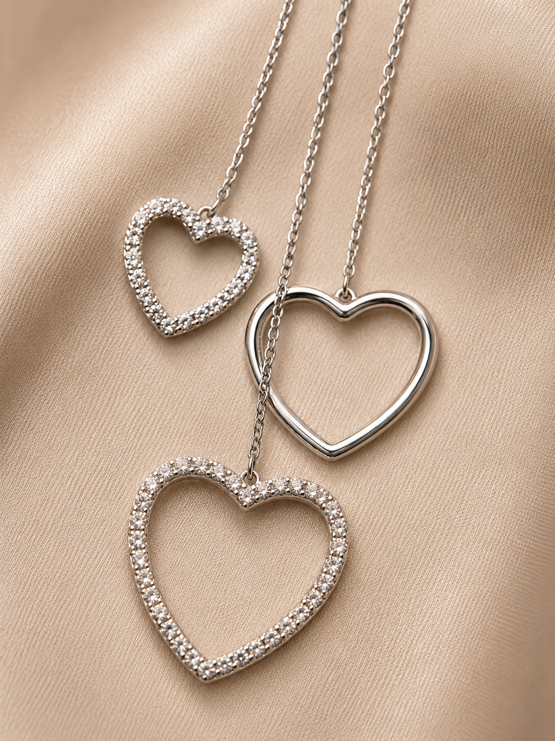 Three silver heart-shaped pendants on a beige fabric background. 925 sterling silver earrings, sterling silver heart studs, silver heart earrings, 925 silver earrings for women, heart stud earrings, cubic zirconia earrings, hypoallergenic earrings, everyday silver jewellery, sterling silver studs, dainty silver earrings, silver jewellery India, Ashaarya