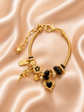 Black Diva anti-tarnish charm bracelet with black crystal heart charm and gold-tone finish. Gold bracelet with black heart charms on a pink satin background