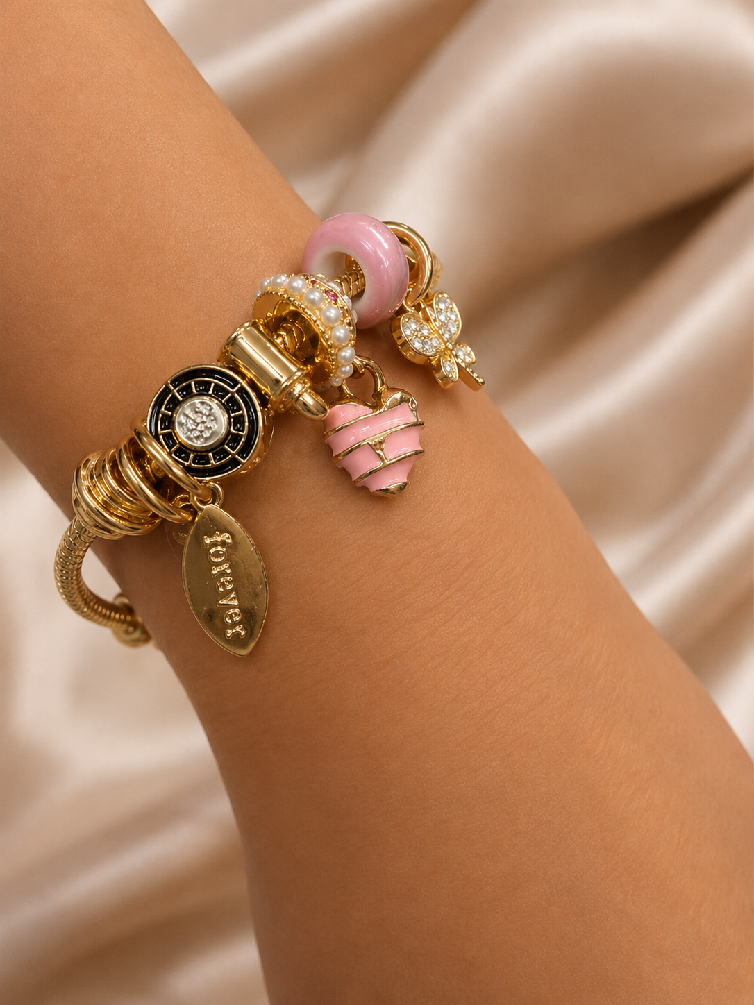 Model wearing Blush Forever Charm Bracelet by Ashaarya crafted in 316L stainless steel with an 18KT gold tone finish. charm bracelet, pink charm bracelet, heart charm bracelet, butterfly charm bracelet, gold charm bracelet for women, anti tarnish jewellery, 316L stainless steel jewellery, lightweight bracelet, skin friendly jewellery, adjustable bracelet, everyday bracelet, demi fine jewellery, comfort jewellery, luxury charm bracelet, Ashaarya charm bracelet