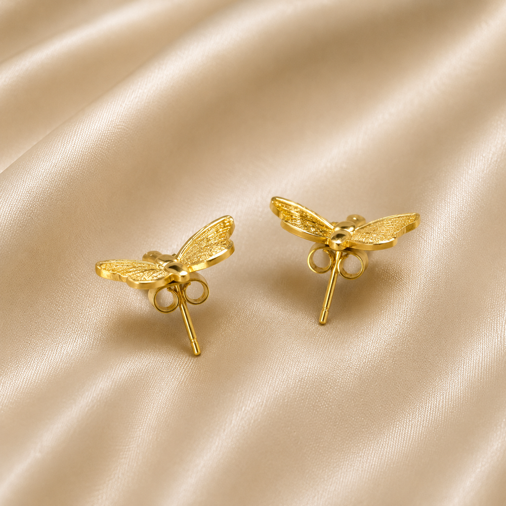 A pair of gold dragonfly stud earrings displayed on a draped beige satin fabric background. anti tarnish earrings, comfort jewellery, butterfly earrings, butterfly stud earrings, gold butterfly earrings, stud earrings for women, lightweight earrings, everyday earrings, stainless steel earrings, hypoallergenic earrings, skin friendly earrings, nature inspired jewellery, minimal earrings, dainty gold earrings, cute earrings for women, butterfly jewellery, anti tarnish jewellery, gold stud earrings, everyday l