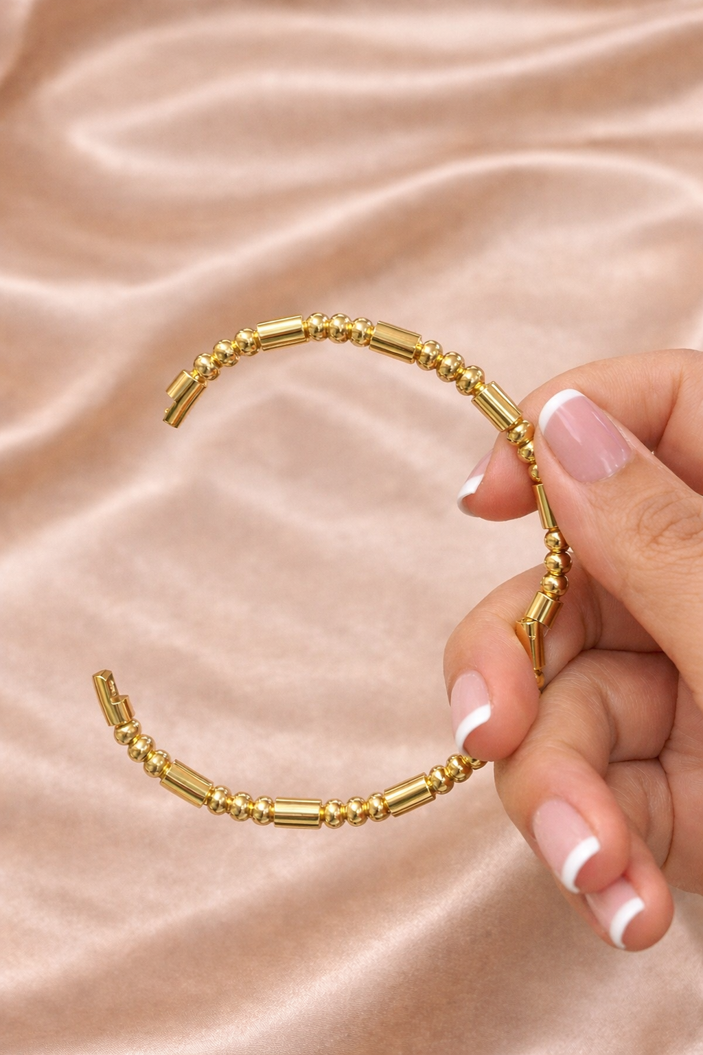 Ashaarya, Ashaarya jewels, ashaarya jewellery, charm bracelets, Gold bracelet held by a hand on a beige fabric background