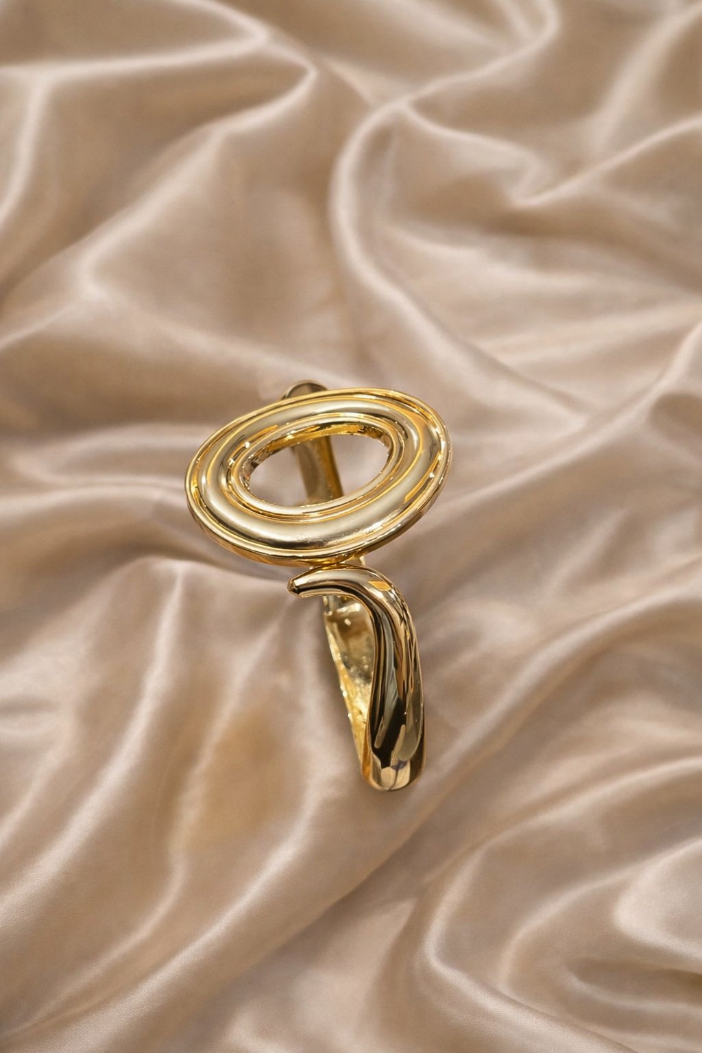 ashaarya, gold bracelet, ashaarya jewels, ashaarya jewellery, charm bracelets, gold bracelet on satin backgroundGold ring with a unique design on a beige satin background
