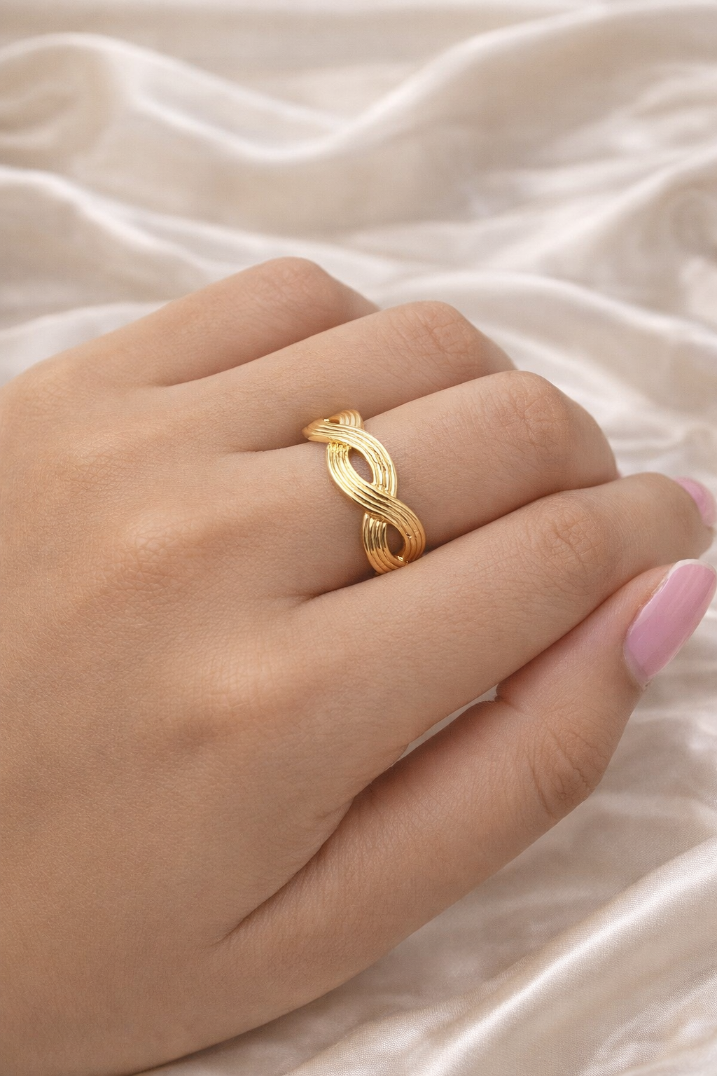Anti-tarnish gold adjustable twist ring with infinity rope design, open back for flexible sizing, displayed on hand against satin background — lightweight comfort jewellery by Ashaarya, Gold ring on a hand with a soft beige background
