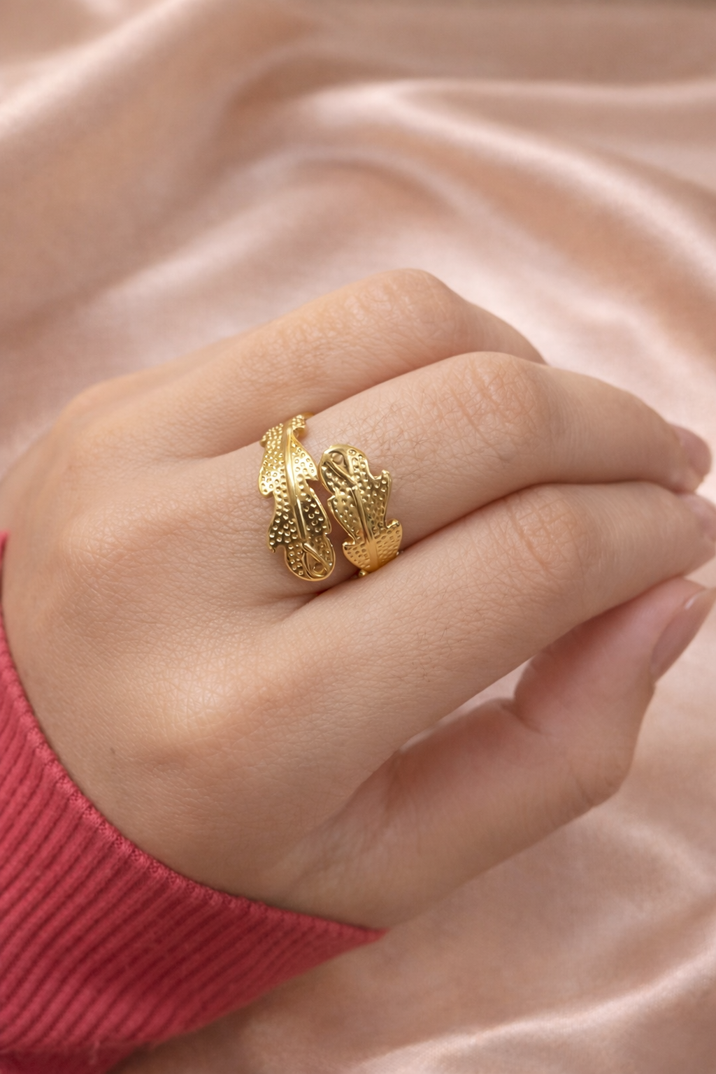 Anti-tarnish gold leaf design ring worn on hand, featuring textured wrap detailing, photographed against champagne satin background — comfort jewellery by Ashaarya. Gold ring on a person's finger against a pink fabric background