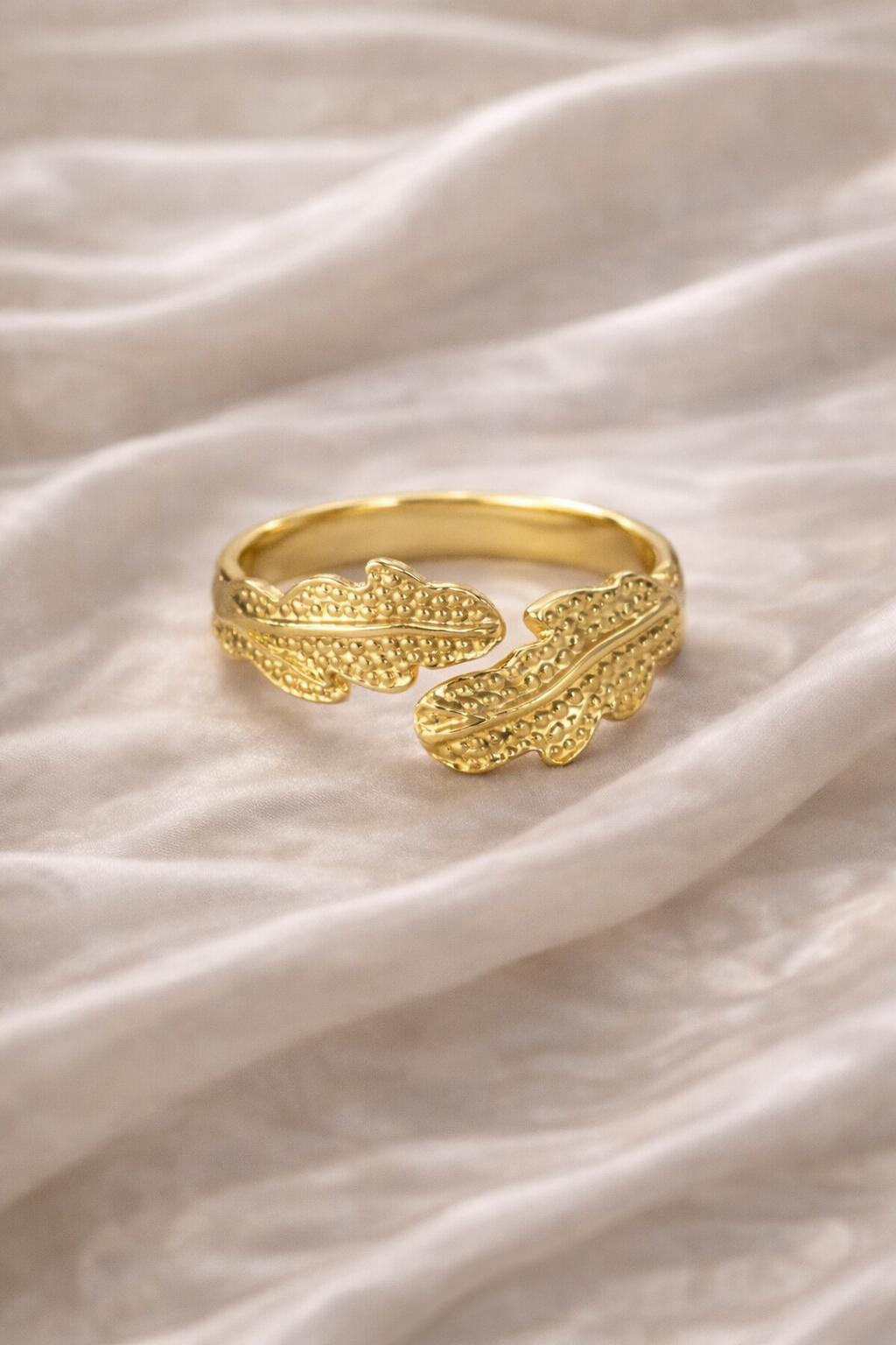 Anti-tarnish gold leaf design ring worn on hand, featuring textured wrap detailing, photographed against champagne satin background — comfort jewellery by Ashaarya. Gold ring with leaf design on a white fabric background