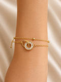 A close-up of a gold double-strand bracelet worn on a wrist, featuring a central interlocking circular design with a clear stone halo, set against a soft beige satin background. Linked in Light anti-tarnish gold bracelet for women with interlocking circular motif and baguette-cut stones by Ashaarya