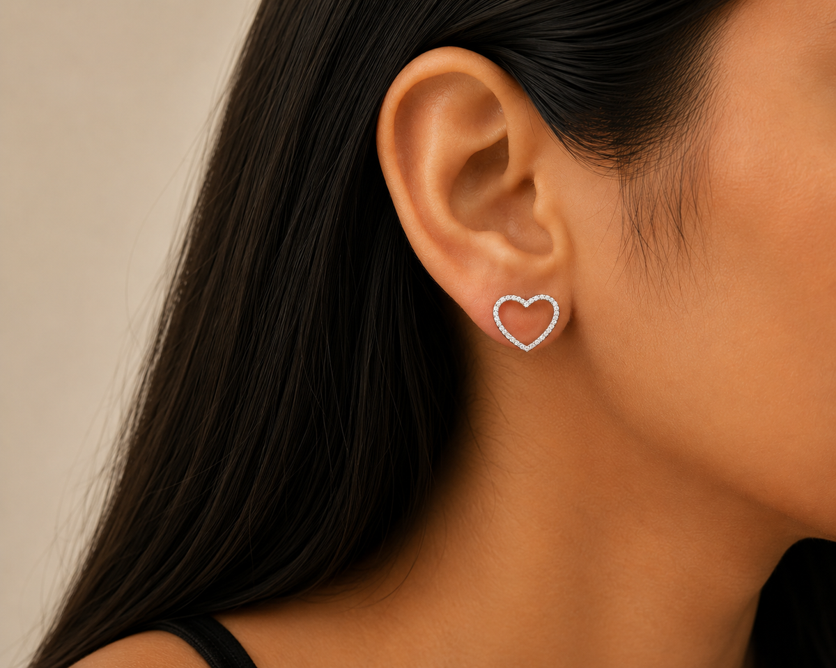 Heart-shaped earrings worn by a person with a neutral background. 925 sterling silver earrings, sterling silver heart studs, silver heart earrings, 925 silver earrings for women, heart stud earrings, cubic zirconia earrings, hypoallergenic earrings, everyday silver jewellery, sterling silver studs, dainty silver earrings, silver jewellery India, Ashaarya