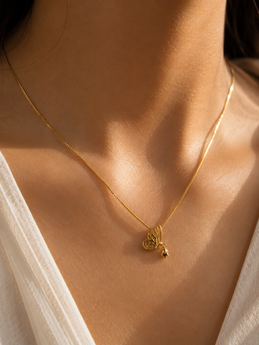 Minimalist gold-tone butterfly necklace styled on a woman's neckline with a white shirt.