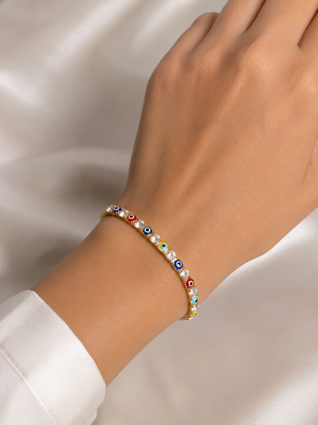 Close-up of multicoloured evil eye motifs and American diamond detailing on Ashaarya's gold-tone bracelet.