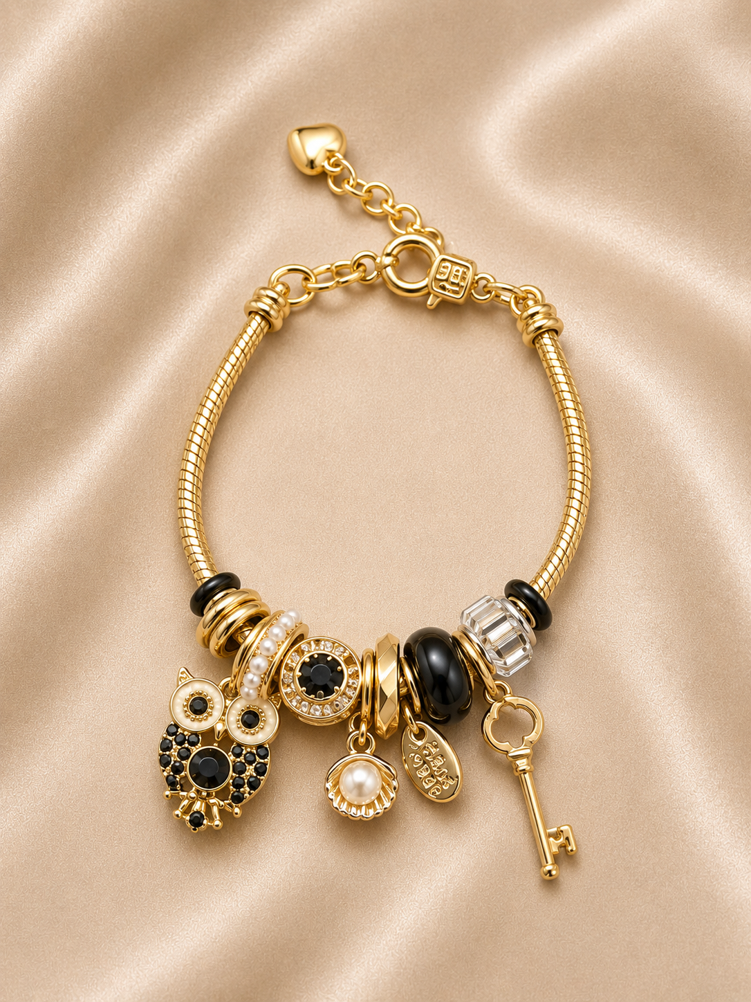 Noir Wisdom Charm Bracelet by Ashaarya featuring owl, key, pearl shell and black crystal charms in 18KT gold plated 316L stainless steel.
