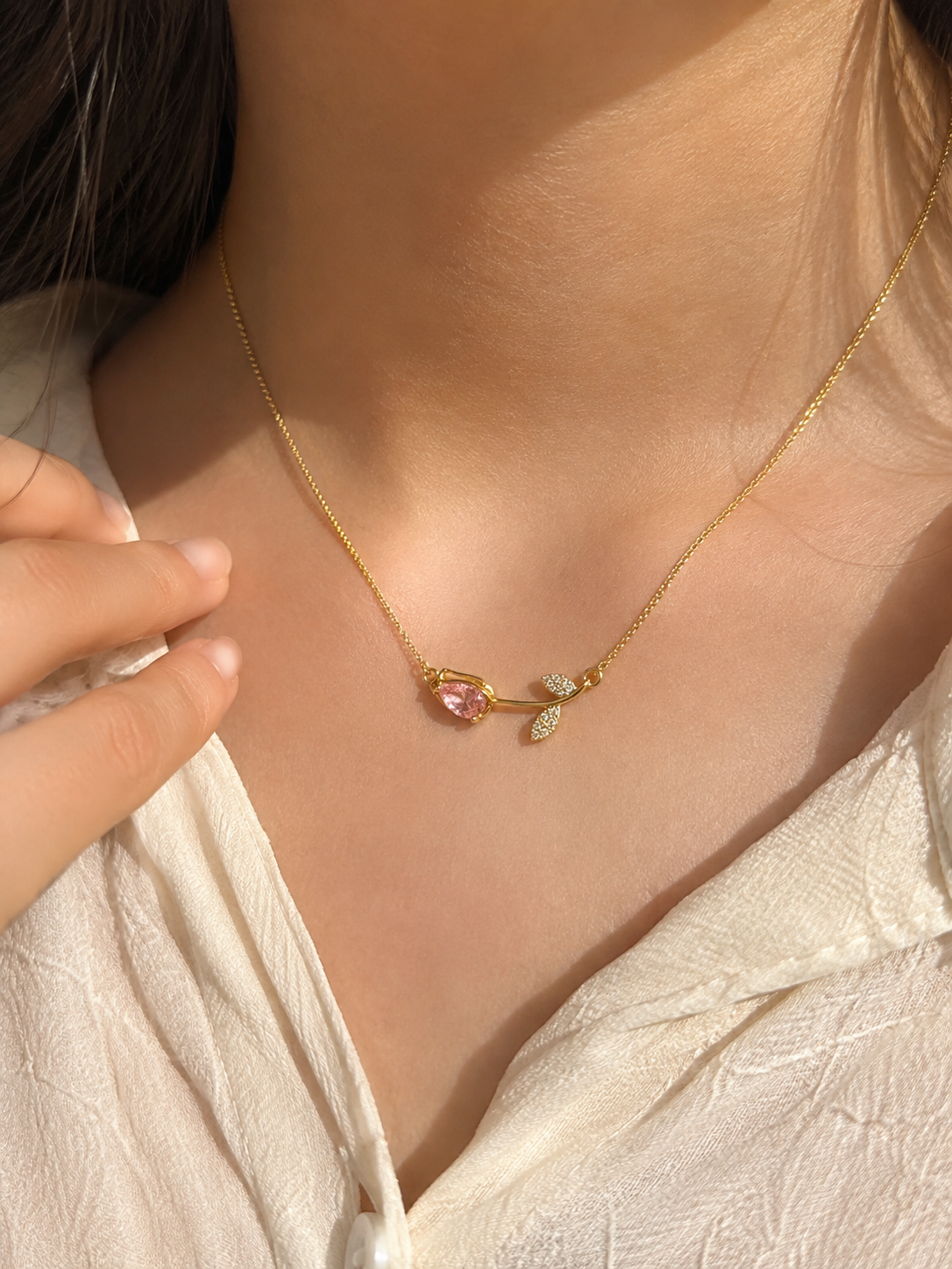 Pink gemstone gold necklace for women featuring a teardrop pink stone and delicate crystal leaf pendant