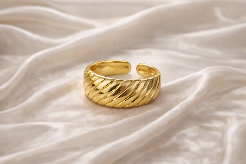 Anti-tarnish spiral gold ring with adjustable open back placed on satin fabric background Gold textured ring on a soft white fabric background