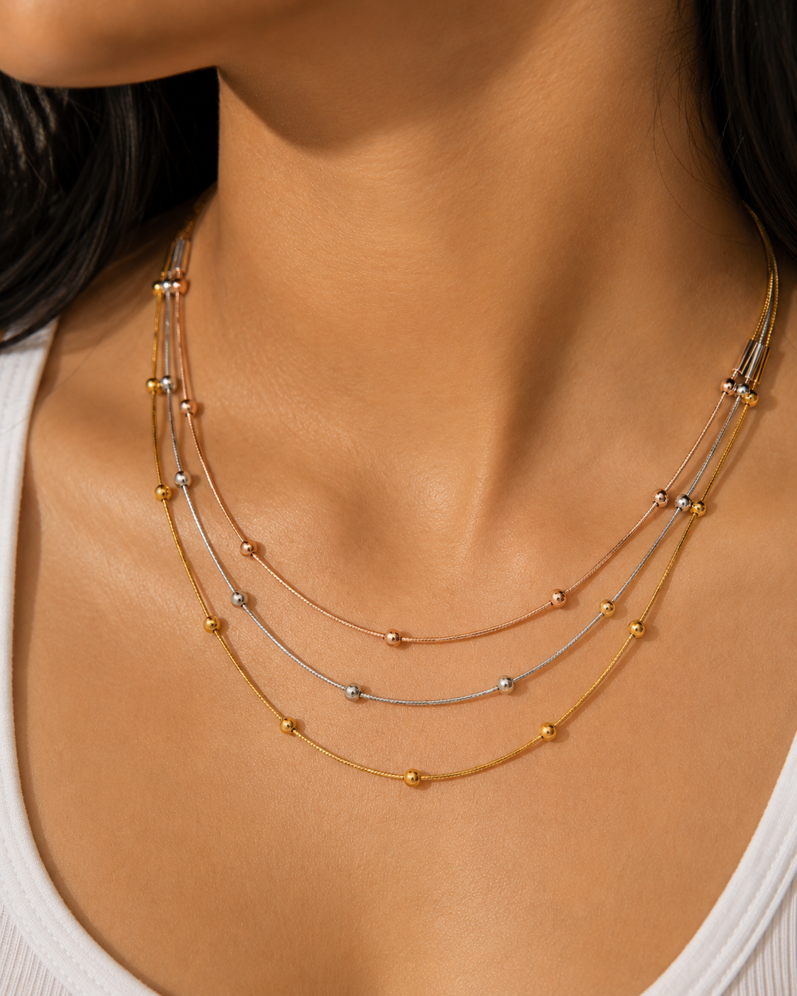 Close-up of a woman wearing a delicate gold necklace with small beads.trio necklace for women, layered necklace, tri colour necklace, three tone necklace, stainless steel necklace, anti tarnish necklace, lightweight necklace, everyday necklace, luxury necklace for women, 18KT gold plated necklace, rose gold necklace, silver necklace, beaded necklace, demi fine jewellery, comfort jewellery, Ashaarya necklace