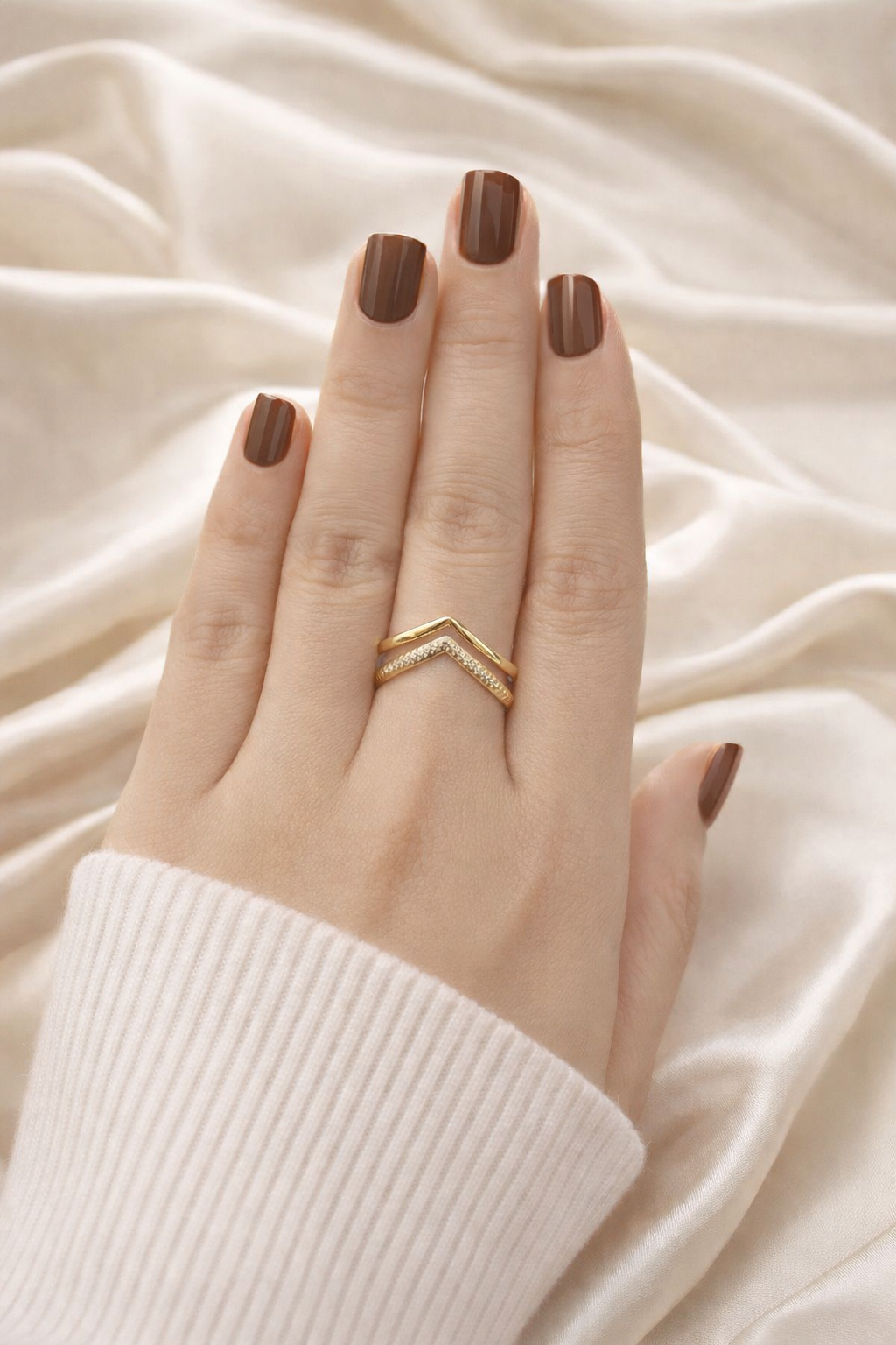 Close up of anti tarnish V shaped adjustable ring with chevron layered design – lightweight comfort jewellery Hand wearing a gold ring with a chevron design on a beige fabric background