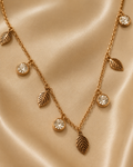A gold-toned necklace with leaf-shaped charms and round clear crystal pendants, displayed on a draped beige satin fabric. rose gold necklace for women, anti tarnish necklace, leaf pendant necklace, nature inspired necklace, lightweight necklace for women, stainless steel necklace, 18kt rose gold necklace, dainty necklace for women, everyday necklace, minimalist jewellery, comfort jewellery, waterproof necklace, skin friendly necklace, Ashaarya necklacebackground.