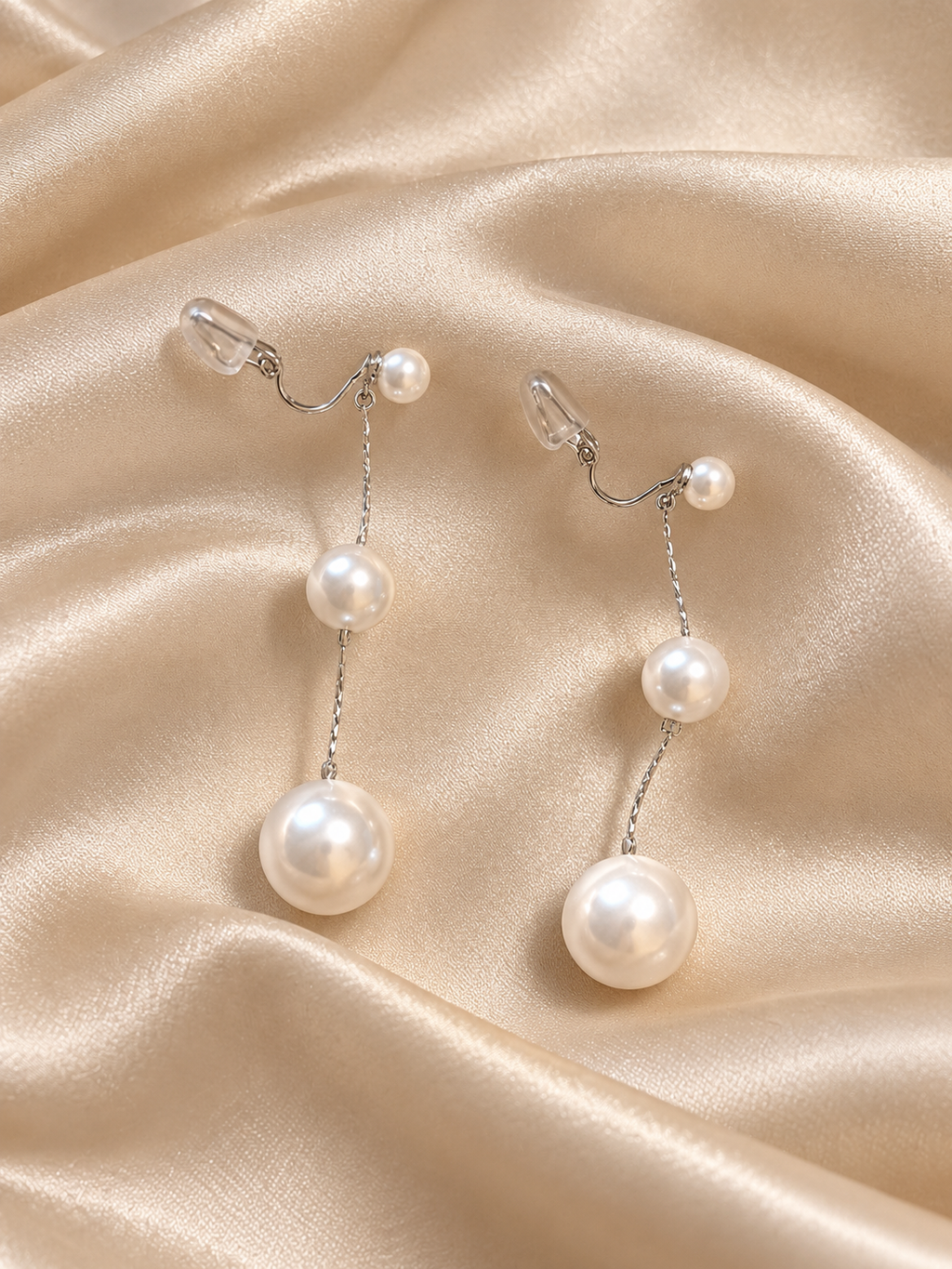 Close-up of white pearl dangling earrings with three graduated pearl accents and fine silver-tone chain detailing.